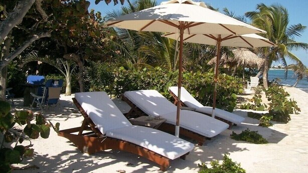 A beachside lounge area with sun loungers and a large umbrella providing shade. - The only and most charming luxury beachfront cottage on the Riviera Maya (Akumal)