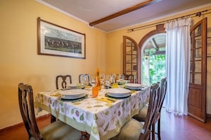 Comedor con mesa preparada para cuatro personas, sillas, un cuadro en la pared y vista a través de un arco.