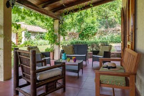 Un patio al aire libre con mobiliario de mimbre, una silla de madera y una mesa con una jarrón y vasos.