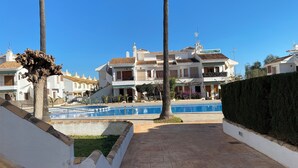Zona de piscina amb un camí empitjorat que condueix a un edifici amb múltiples balcons i un teulat enrajolat.