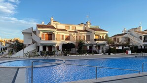 Una gran piscina amb zona de solàrium enrajolat, envoltada per un edifici de diverses plantes amb balcons i teulada enrajolada.