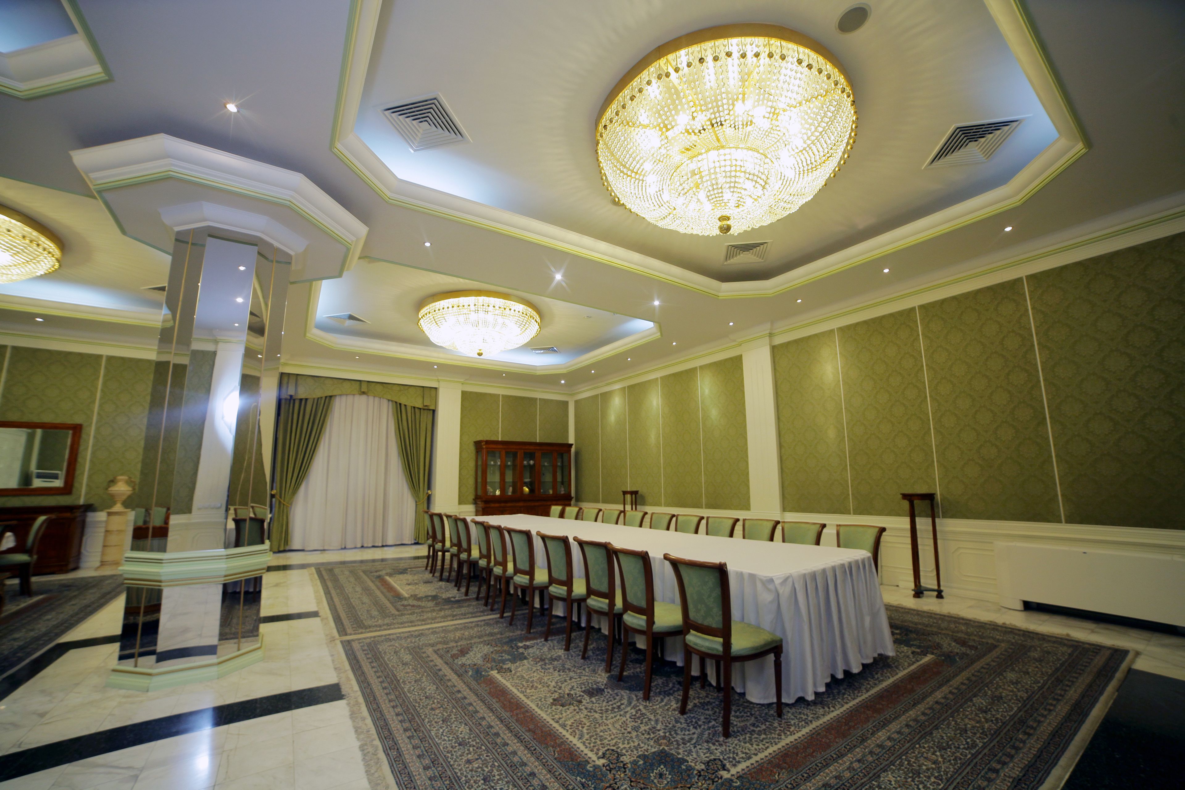 A formal dining room with a long table, chairs, chandeliers, and a decorative column.