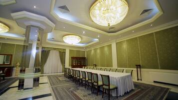 A formal dining room with a long table, chairs, chandeliers, and a decorative column.