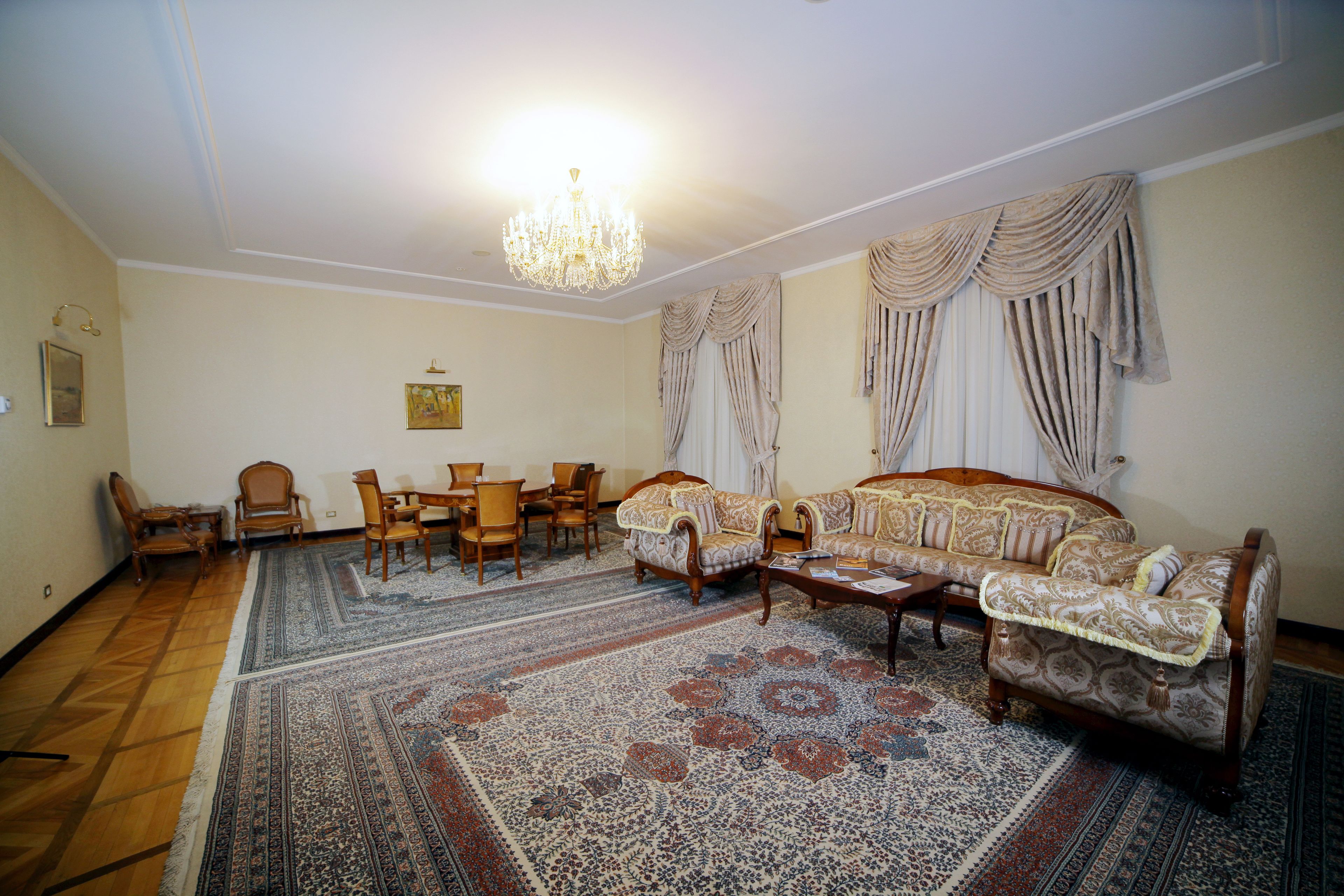 A spacious living room with a large sofa set, wooden chairs, a coffee table, and a patterned rug.