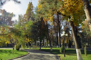 A park with a paved path, trees with yellow leaves, and a street lamp. - Residence Park Hotel (Tashkent)