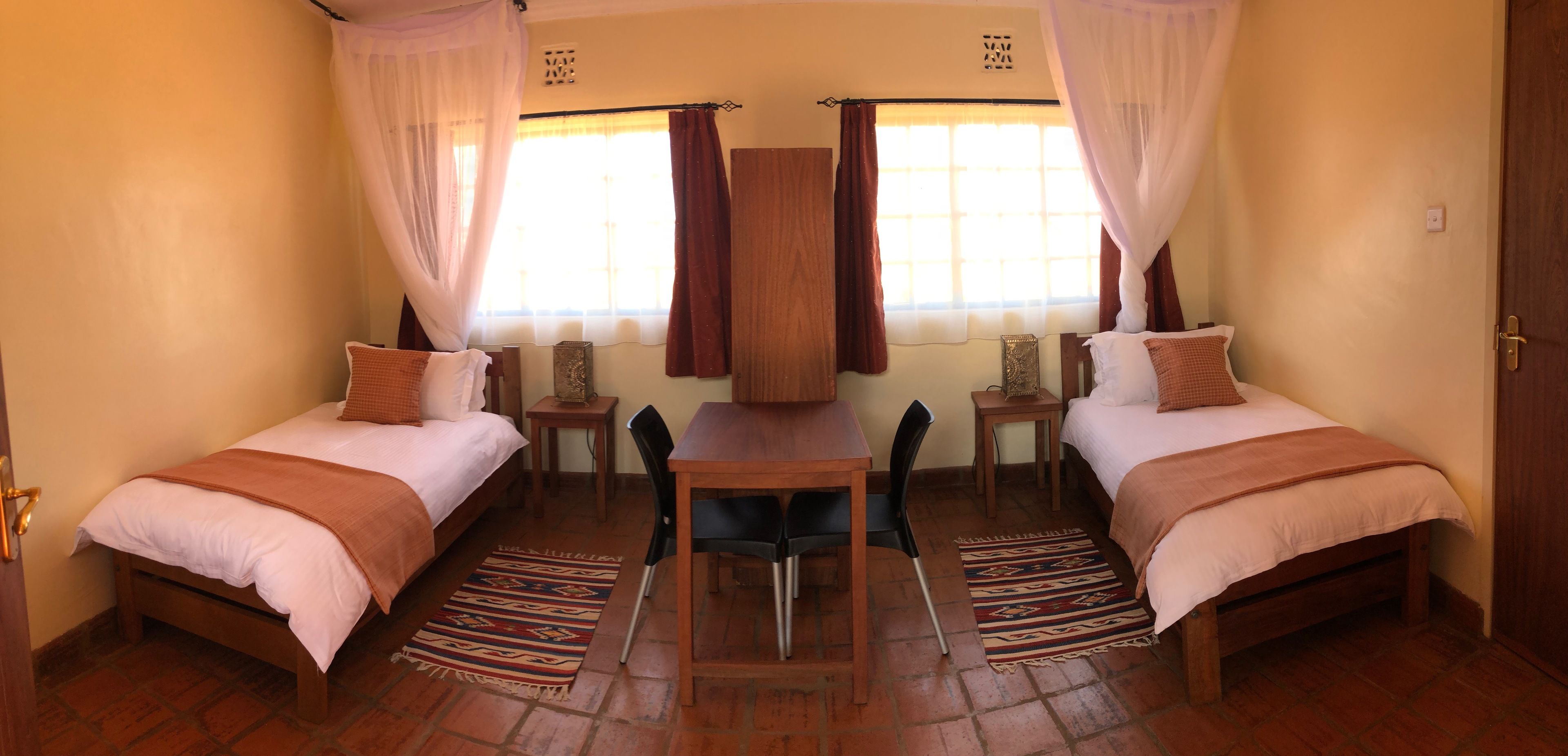 Quarto com duas camas, uma mesa, cadeiras e janela com cortinas.