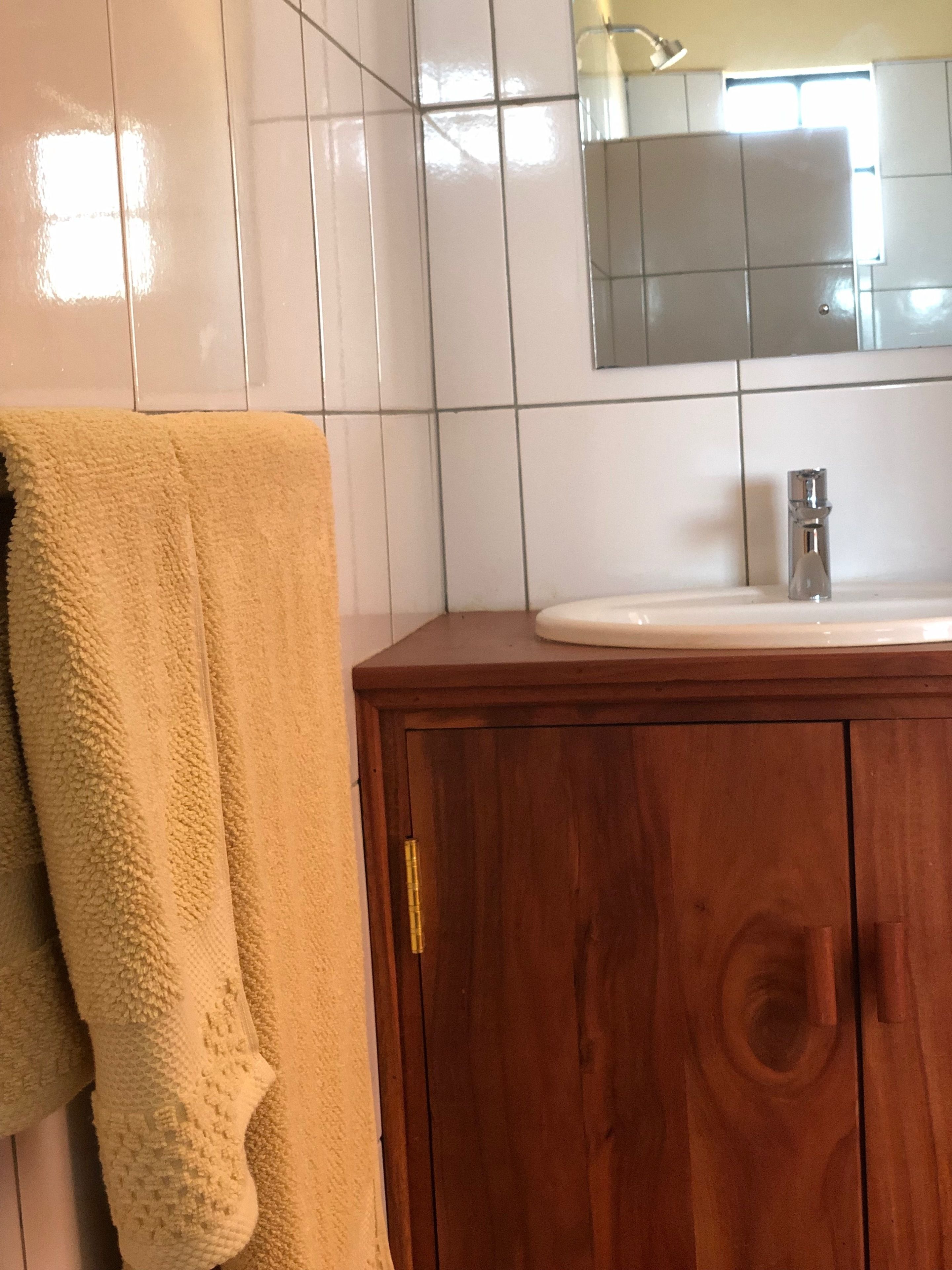 A bathroom with white tiled walls, a wooden vanity with a sink, and a towel hanging on the wall.