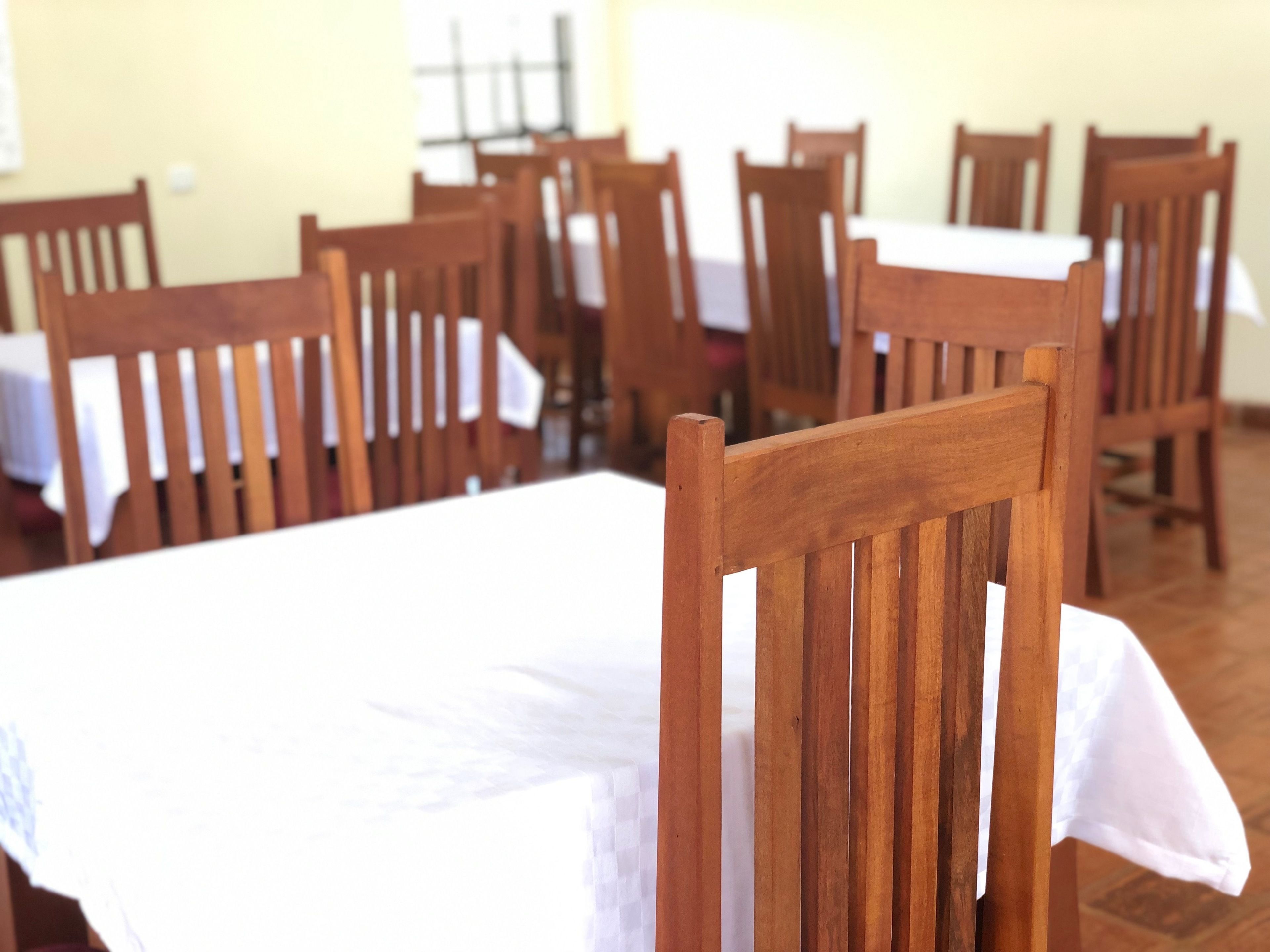 A dining area with wooden tables and chairs, some with white tablecloths.