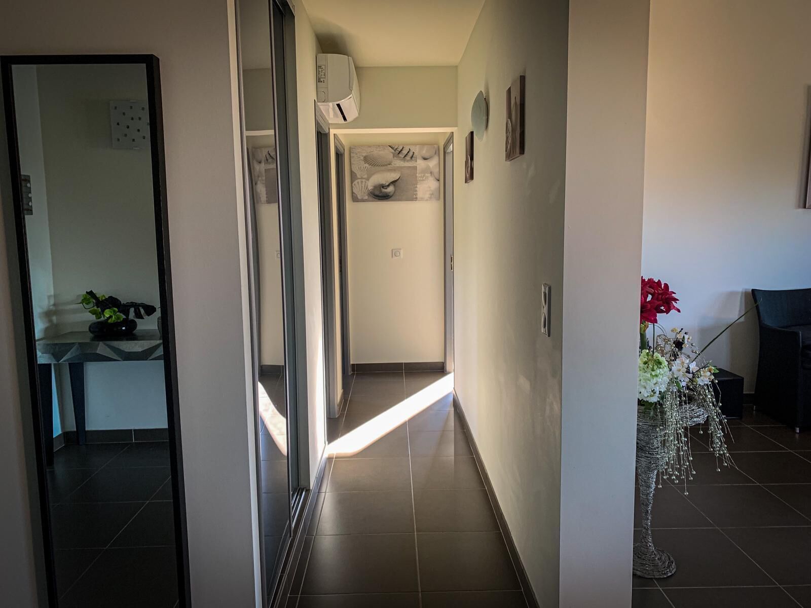 A hallway with a tiled floor, a door with a frosted glass panel, and a wall-mounted air conditioning unit.