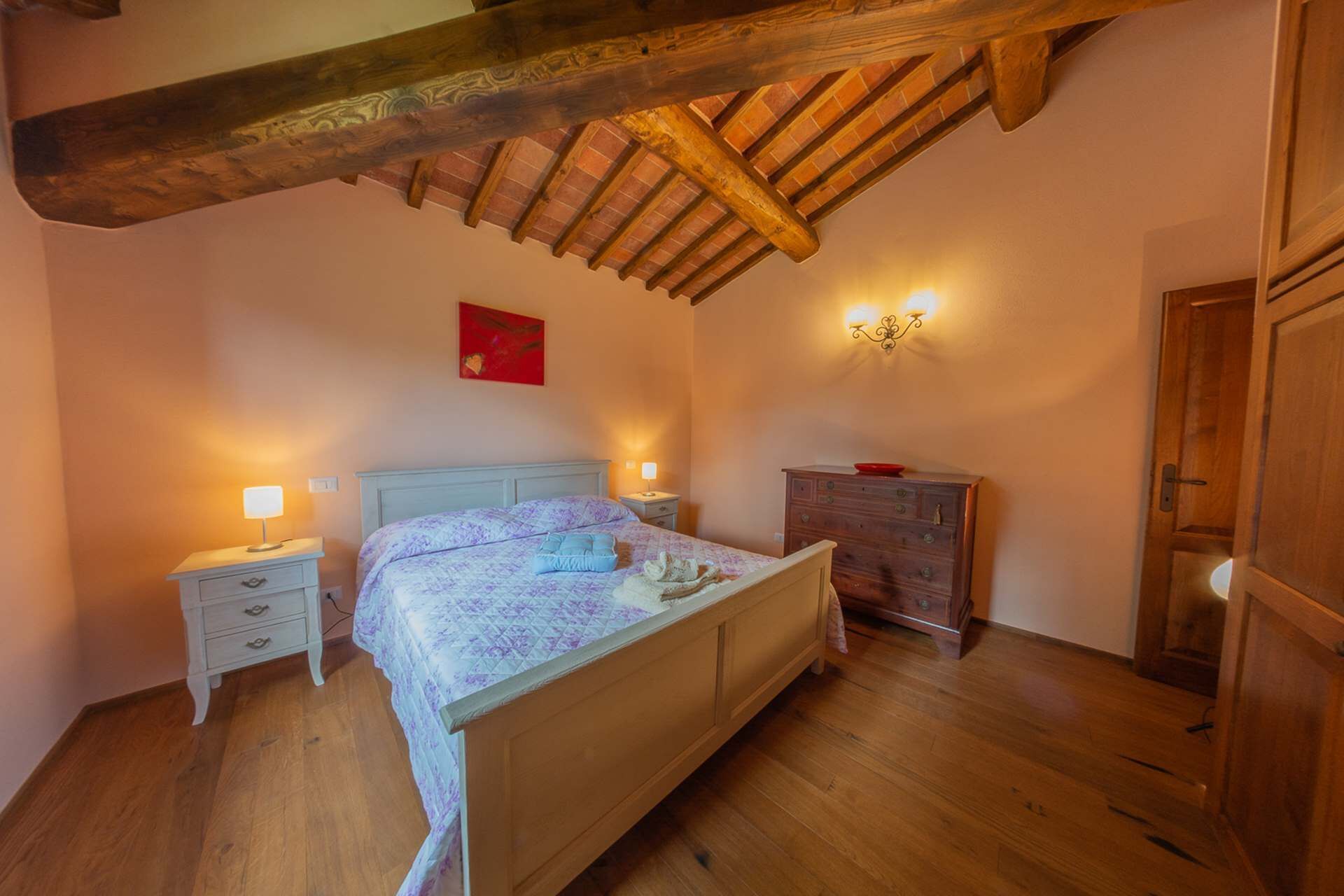 Un dormitorio con una cama de madera, mesitas de noche, un aparador y un cuadro rojo en la pared.