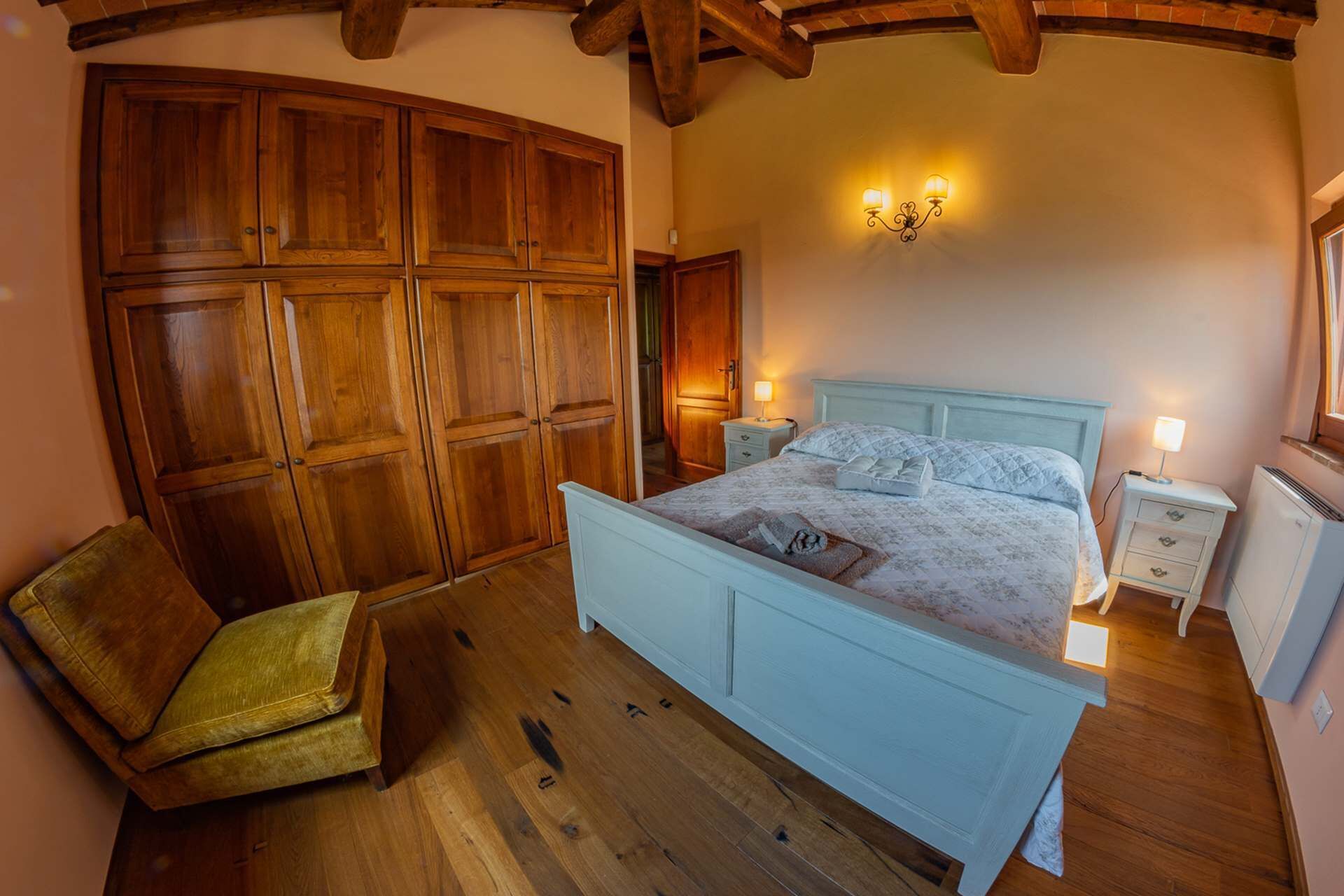Un dormitorio con un armario de madera, una cama con colcha, una mesita de noche, una lámpara y un radiador.