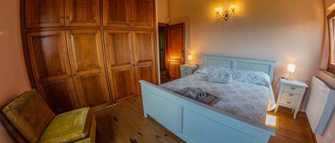 Un dormitorio con un armario de madera, una cama con colcha, una mesita de noche, una lámpara y un radiador.