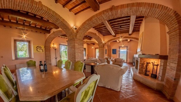 A spacious dining area with a long table and multiple chairs, brick arches, and a fireplace.