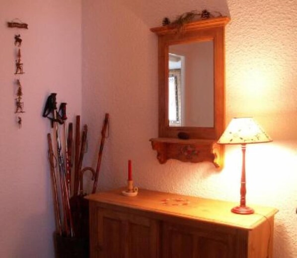 Une console en bois, avec un miroir au-dessus, une bougie rouge et une lampe sur la droite.