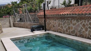 Une piscine rectangulaire à l’eau d’un bleu limpide, entourée d’un mur de pierre et surmontée d’un toit en tuiles.