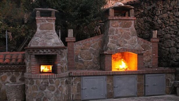 Une cuisine extérieure en pierre, dotée d’un foyer et de deux armoires en métal.