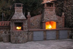 Une cuisine extérieure en pierre, dotée d’un foyer et de deux armoires en métal.