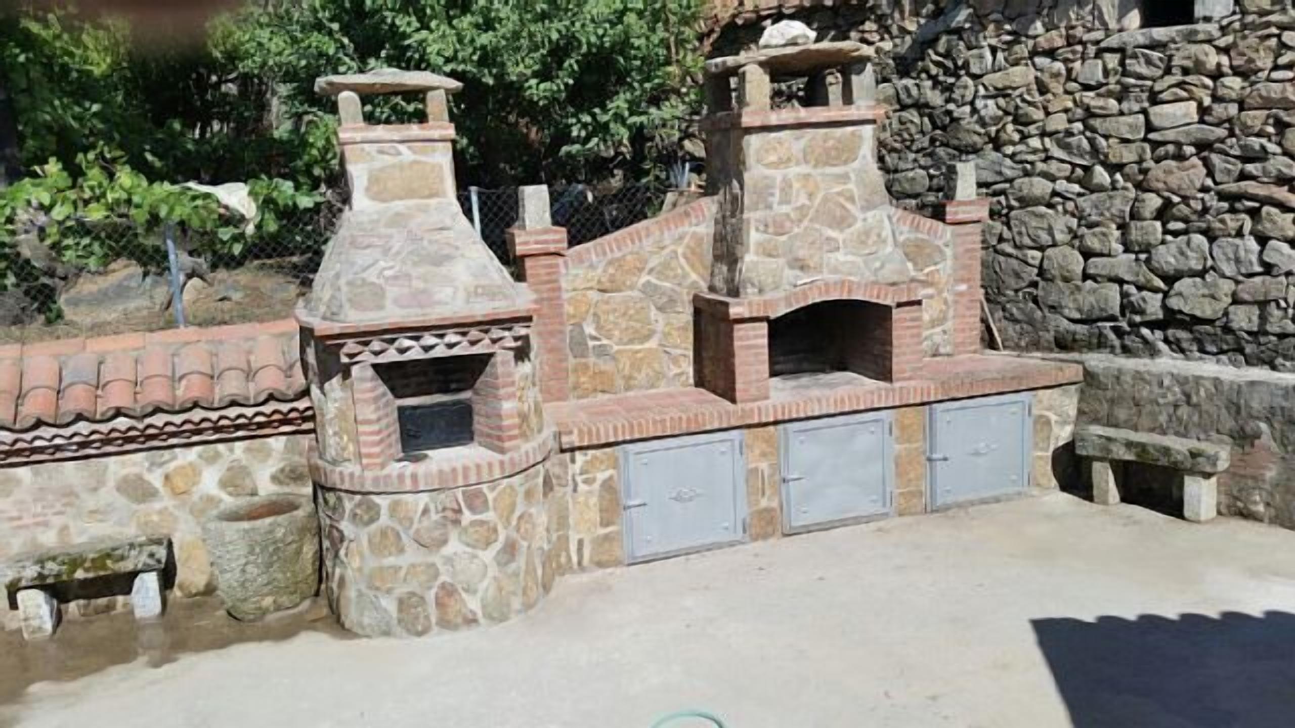 Een buitenkeuken van natuursteen met twee schoorstenen en een ingebouwde grillplaats.
