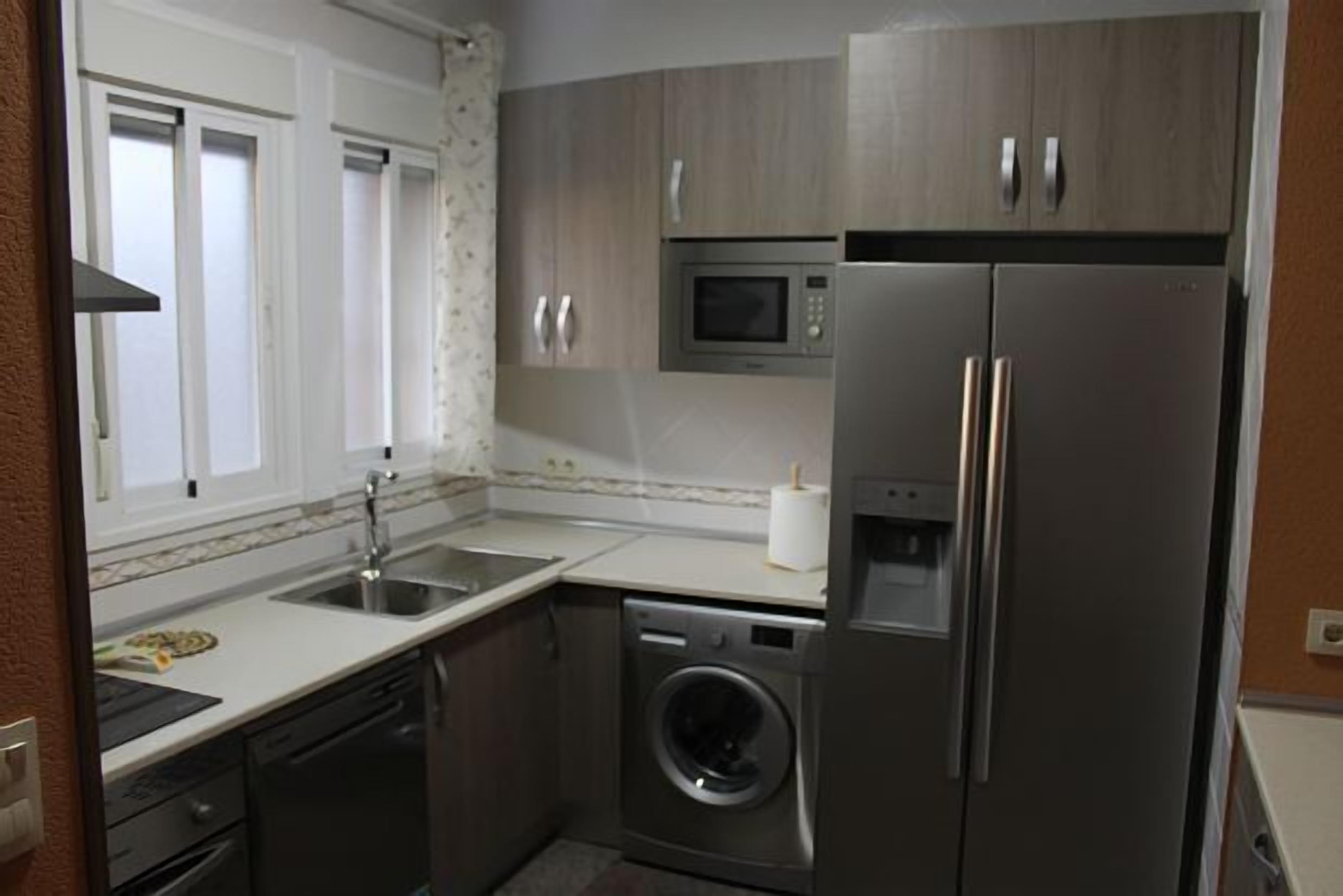 A compact kitchen with a stainless steel refrigerator, microwave, and washing machine.