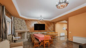 Un coin repas agrémenté d’une cheminée en pierre, d’un téléviseur fixé au mur et d’un lustre.
