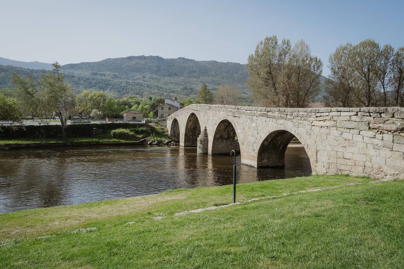 A stone bridge over a river with a grassy bank and trees in the background.