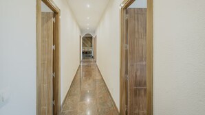 Un couloir avec des portes en bois, un sol carrelé et une vue sur une pièce où se trouve un lit.
