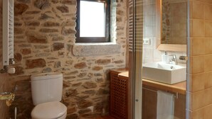 Ein Badezimmer mit Steinwand, einem Fenster, einer Toilette, einem Waschbecken und einer Duschkabine.