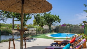 A poolside area with lounge chairs, a table, and a thatched umbrella.