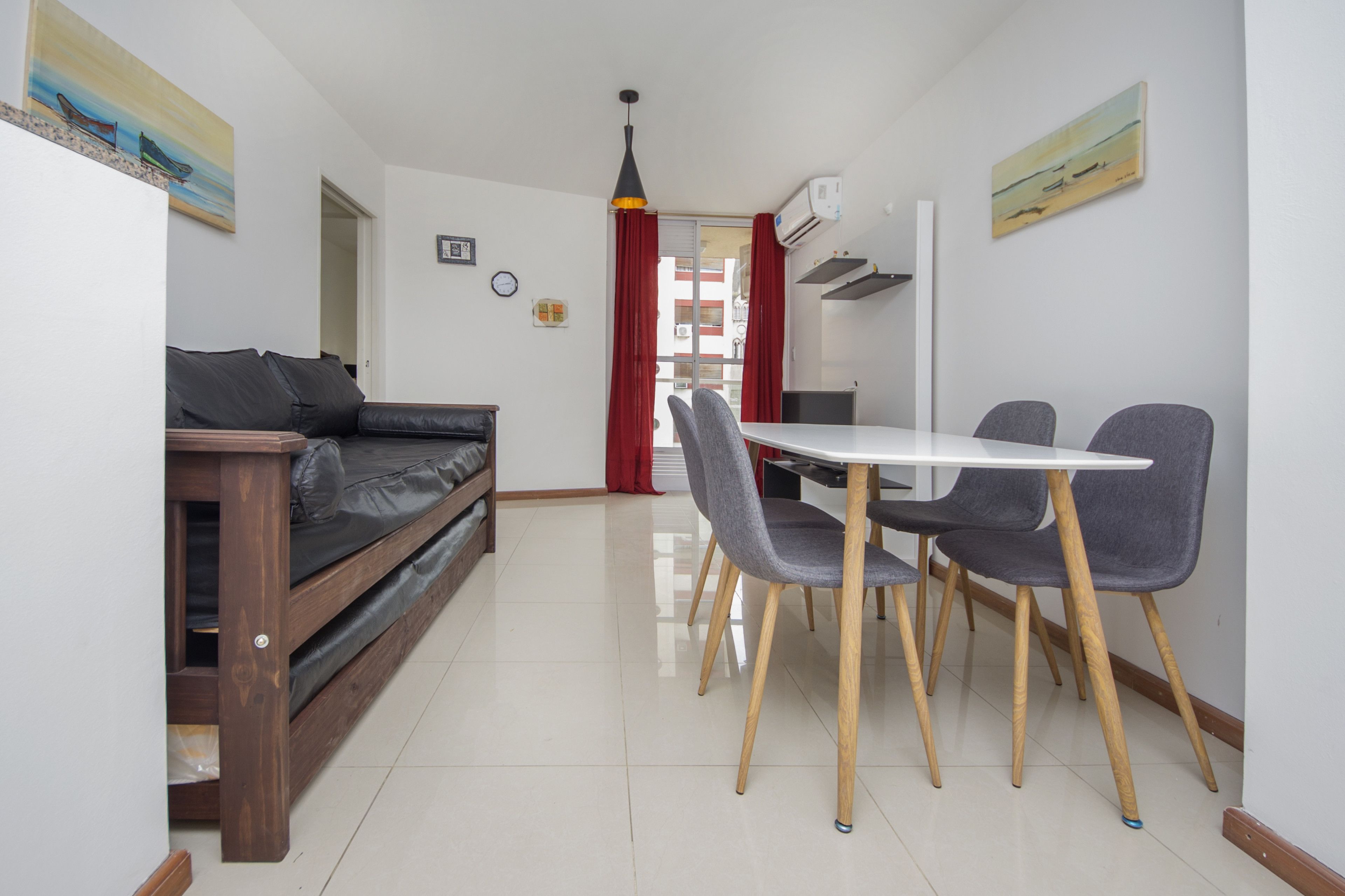 Een moderne woonkamer met een bank, een eettafel en stoelen. Er is een rood gordijn, een klok en kunstwerken aan de muren.