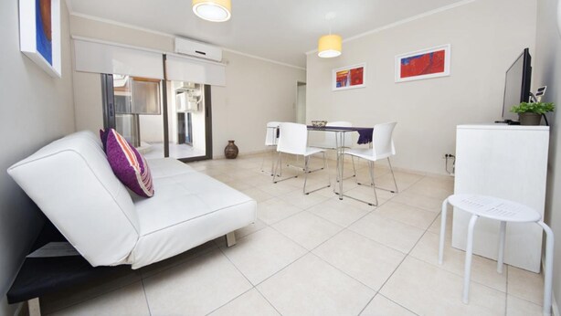 Een moderne, goed verlichte kamer met een witte bank, een eettafel met stoelen en een klein, wit tafeltje.