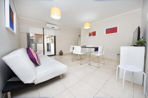 Een moderne, goed verlichte kamer met een witte bank, een eettafel met stoelen en een klein, wit tafeltje.