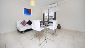 Een ruimtelijk ingerichte leefruimte met een witte bank, een glazen eettafel en een gele hanglamp.