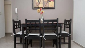 Un coin repas comprenant une table rectangulaire et six chaises, chacune agrémentée d’un coussin blanc. Un vase rempli de fleurs est posé sur la table.