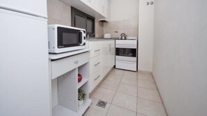 Une cuisine compacte avec des meubles blancs, un four à micro-ondes, une bouilloire et un petit four.