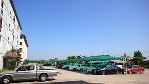 A parking lot with several cars, a building with multiple floors, and a green-roofed structure in the background. - Matini Amata (Phan Thong)