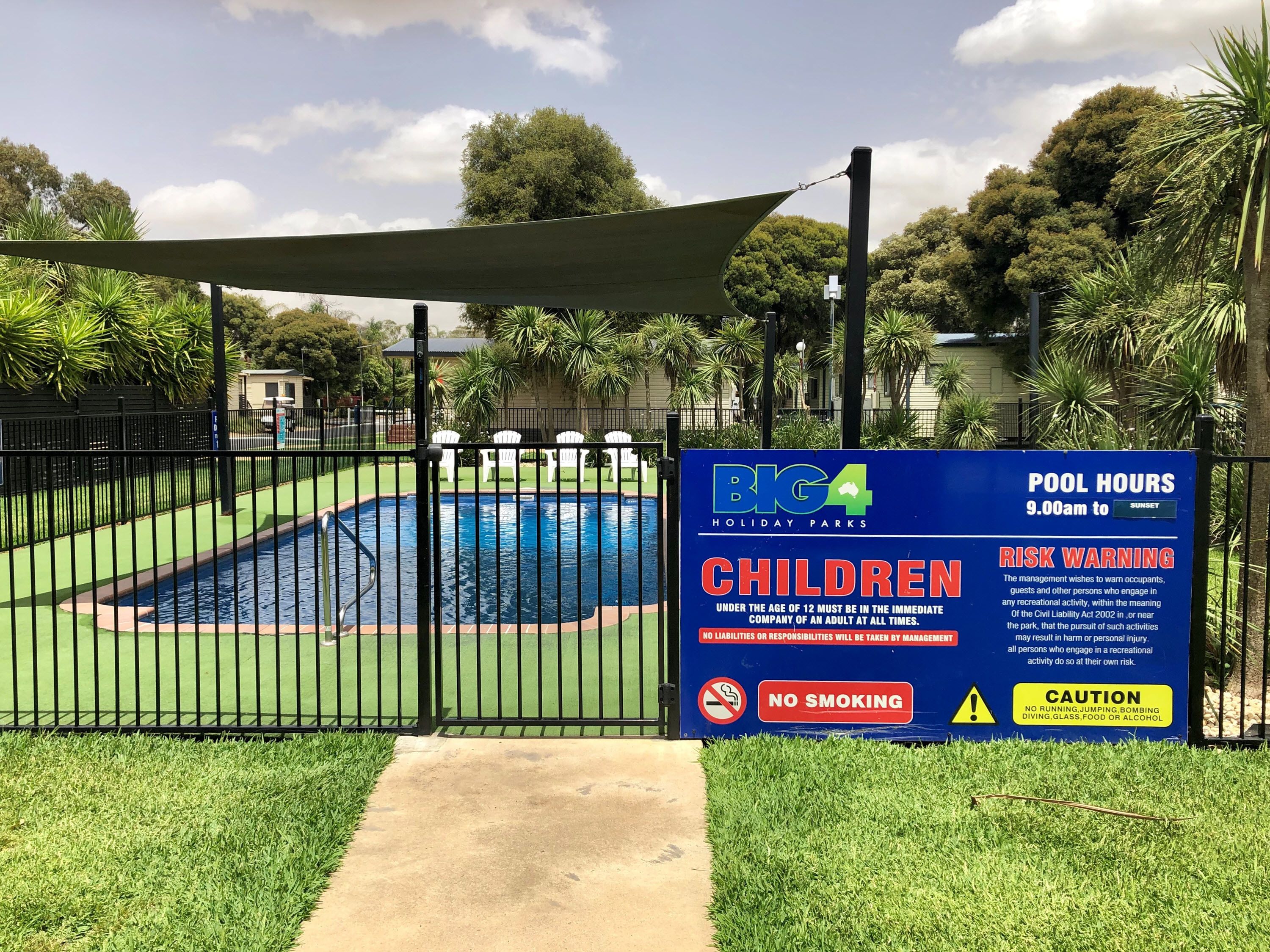 A pool area with a sign indicating pool hours from 9:00 am to sunset, a no smoking zone, and a caution against running, jumping, and other activities.