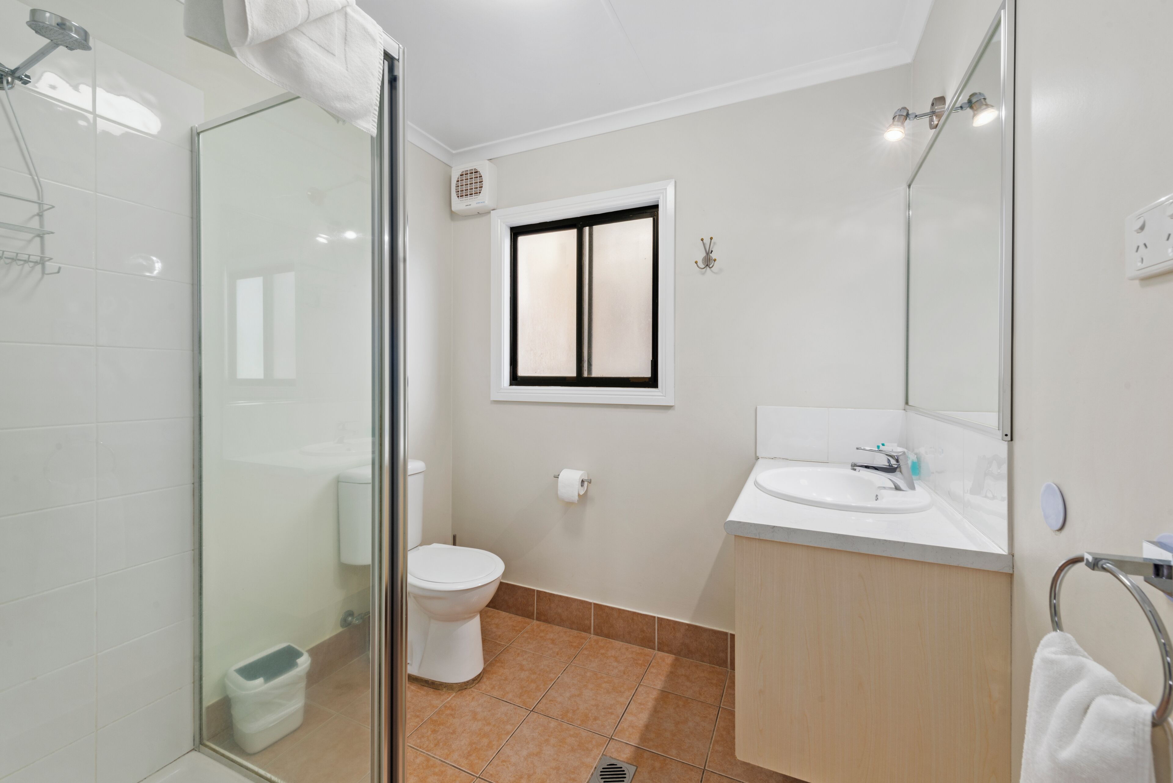 A modern bathroom with a glass shower enclosure, a toilet, a sink, and a window.
