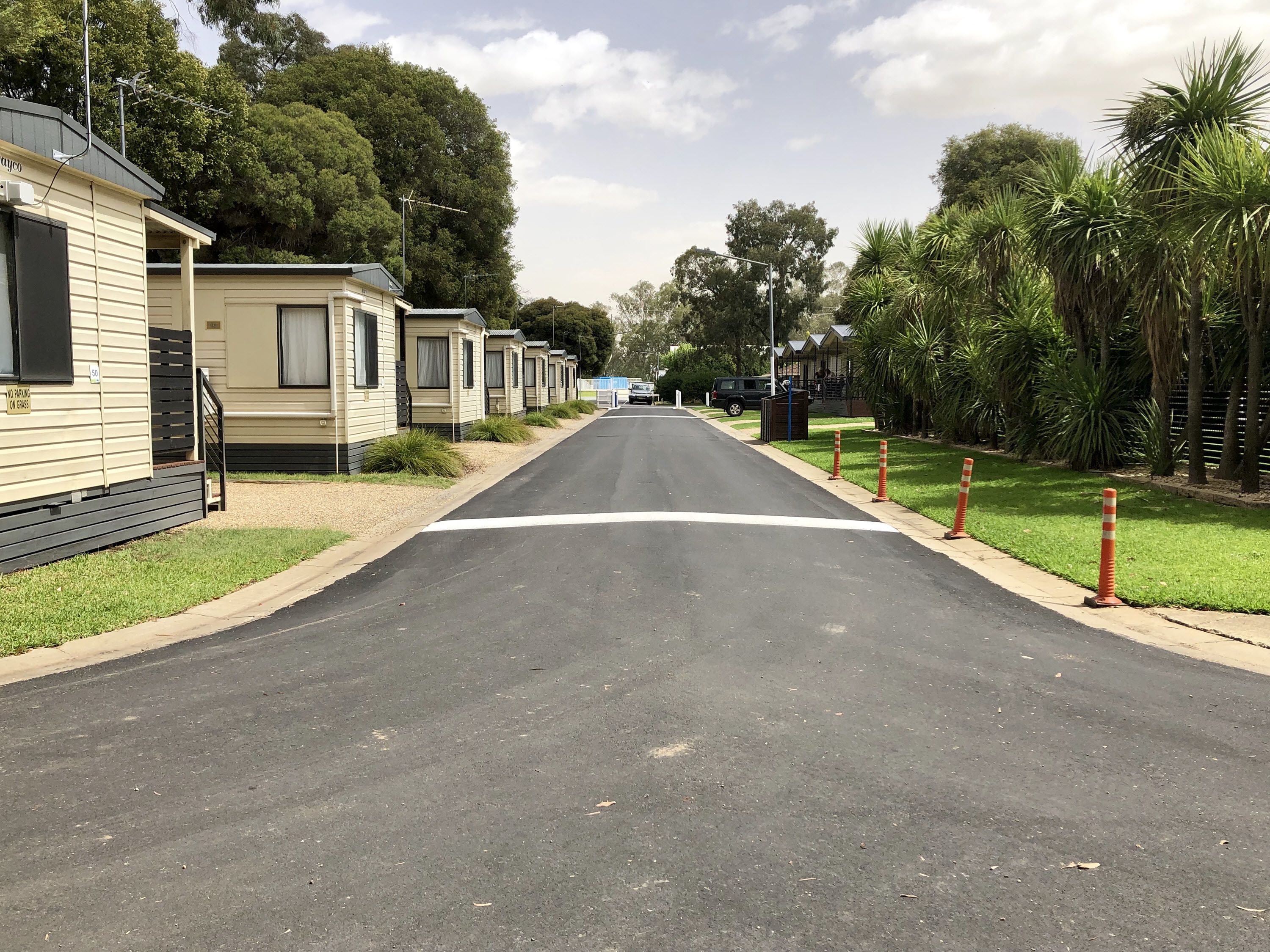 A row of mobile homes with a clear road in front, surrounded by greenery and trees.