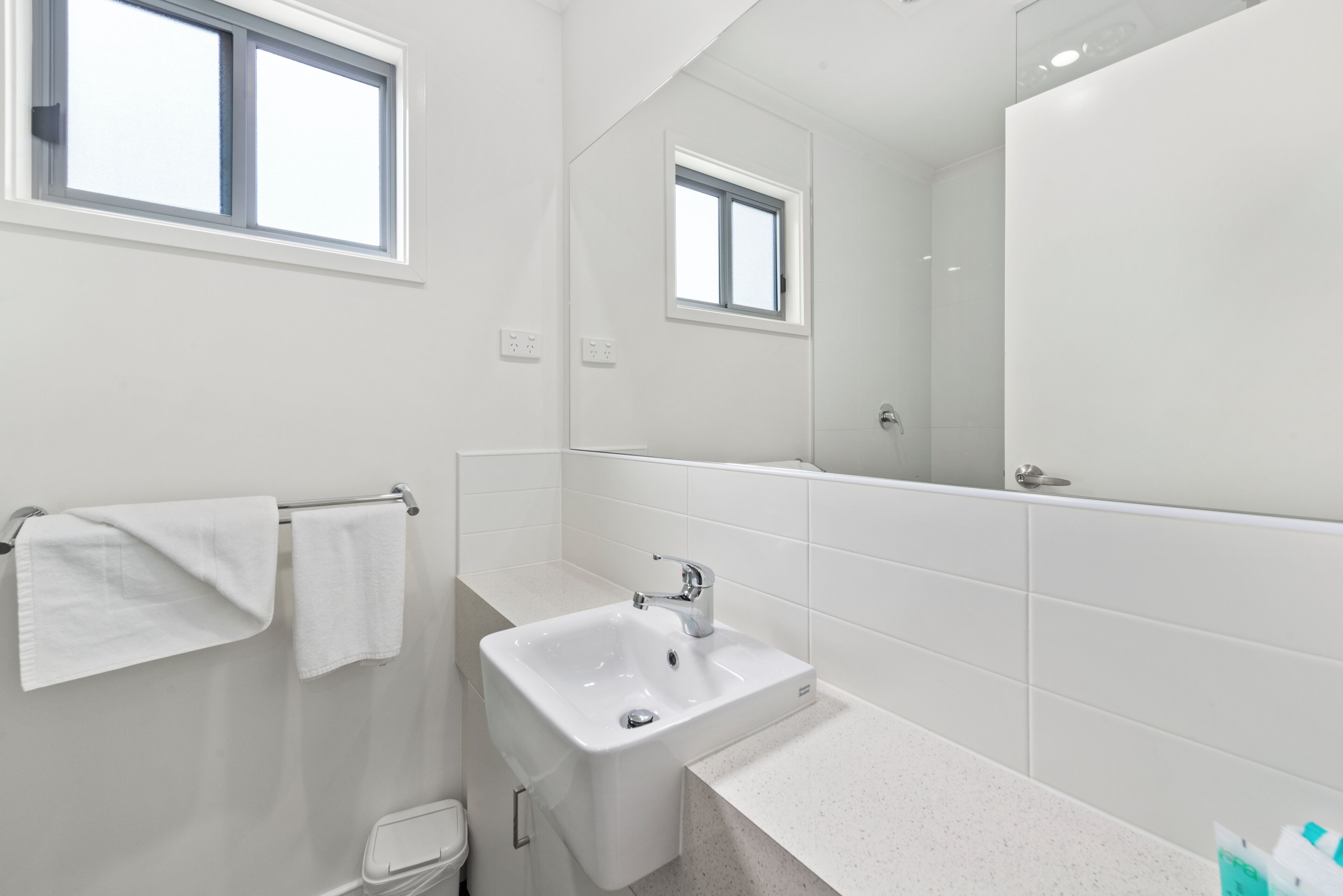 A modern bathroom with a white sink, a mirror, and a window.