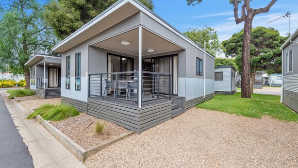 Une maison mobile moderne dotée d’un porche couvert, d’une petite terrasse et d’une allée en gravier.