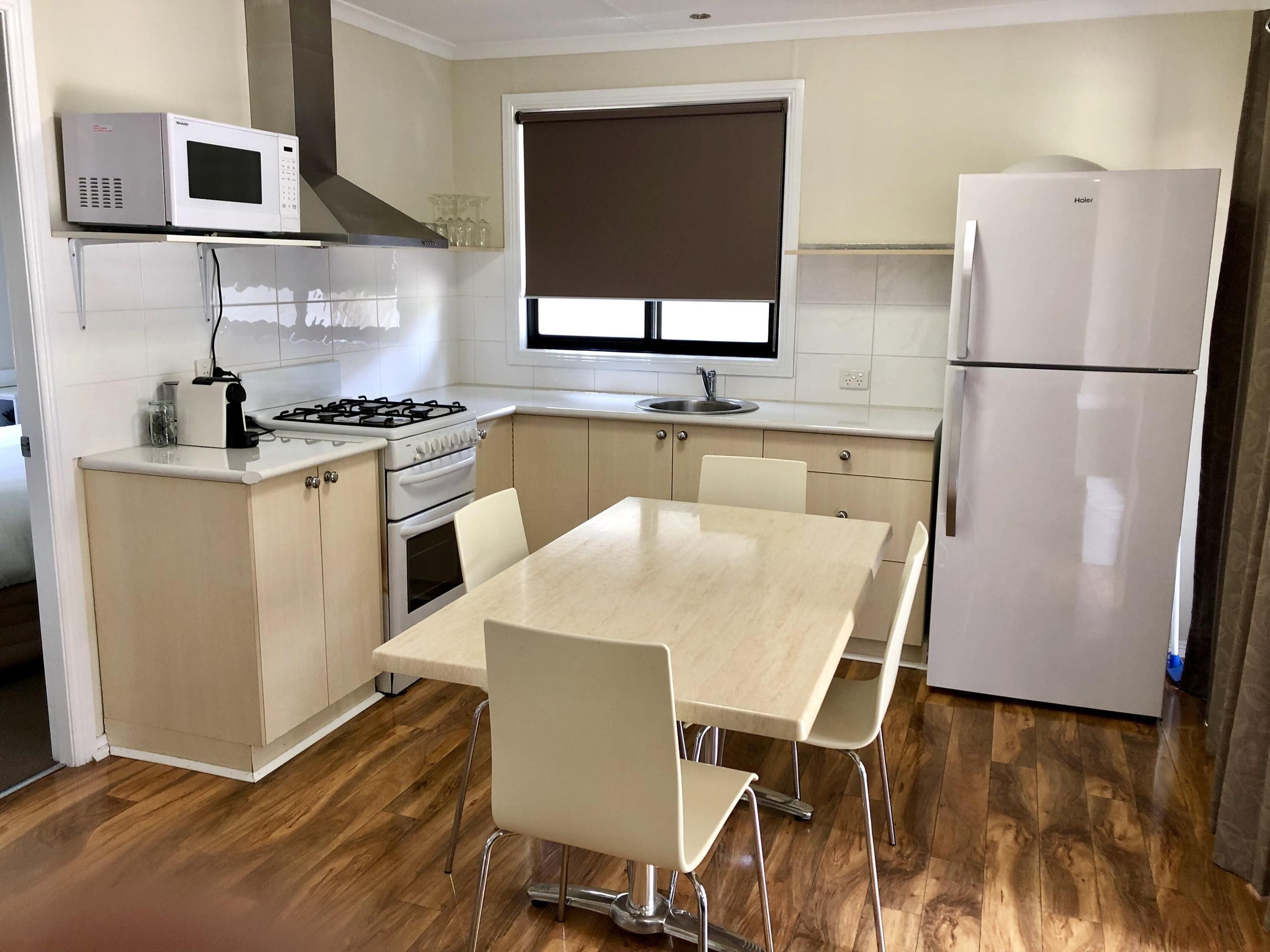 A compact kitchen with a gas stove, microwave, refrigerator, and a dining area with a table and chairs.