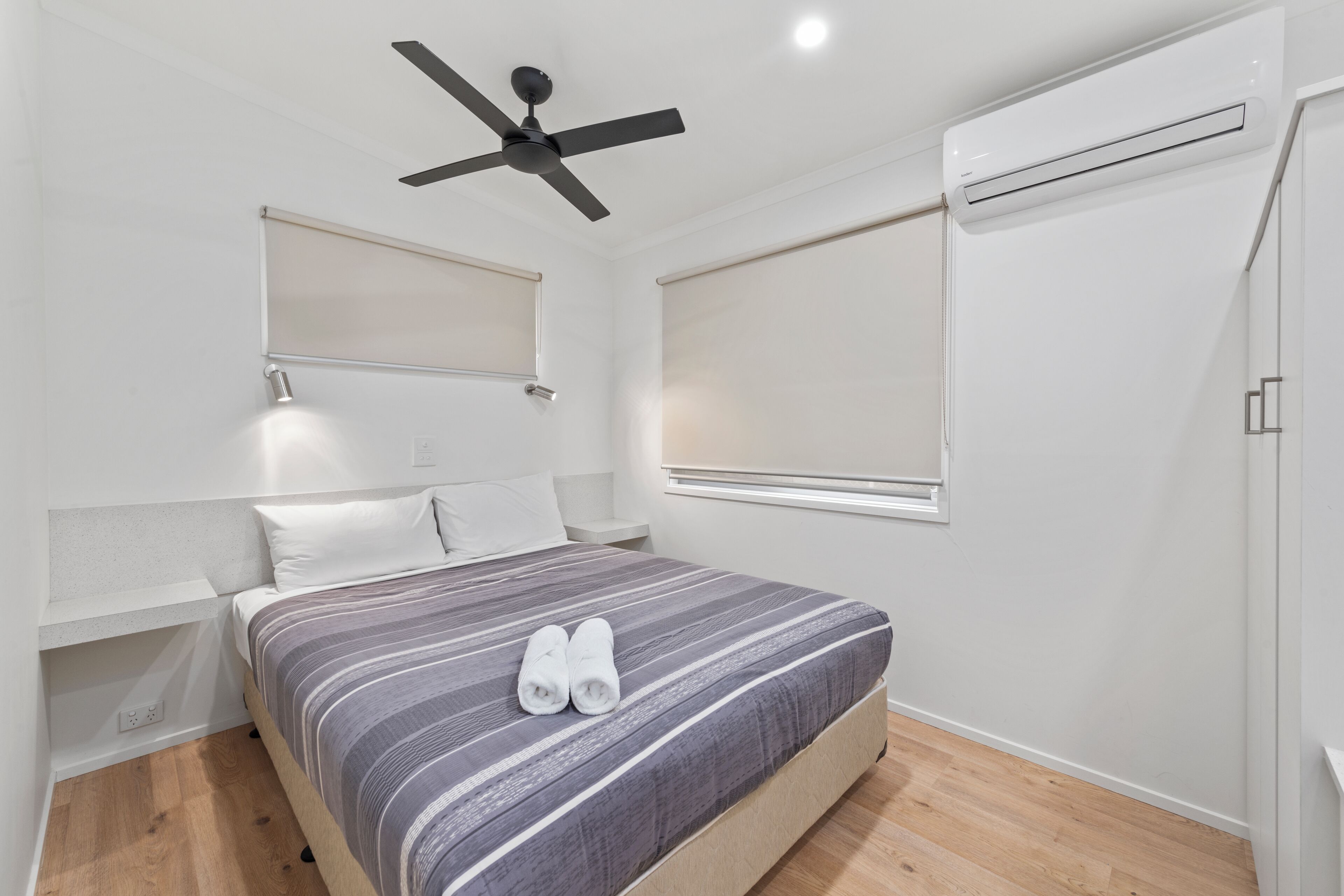 A modern bedroom with a bed, a ceiling fan, an air conditioning unit, and a window with blinds.