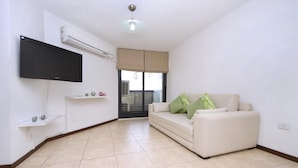 A living room with a flat-screen TV mounted on the wall, a beige sofa with green cushions, and a tiled floor. - Fragueiro Flat BU6 (Córdoba)