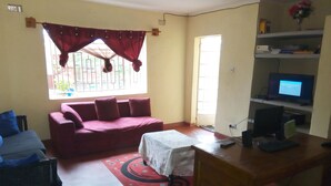 A living room with a red sofa, a small table, a TV, and a computer desk. - Lodge B Mawira (Liwonde)