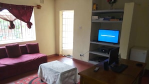 A living room with a sofa, a small table, a TV, and a computer on a desk. - Lodge B Mawira (Liwonde)