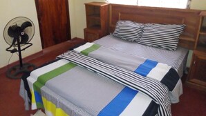 A bedroom with a bed, a fan, a wooden door, and a window with curtains. - Lodge B Mawira (Liwonde)