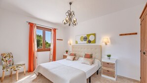 A bedroom with a large bed, a chair, a nightstand, a lamp, and a window with curtains. - Casa Las Vías (Petra, Mallorca)