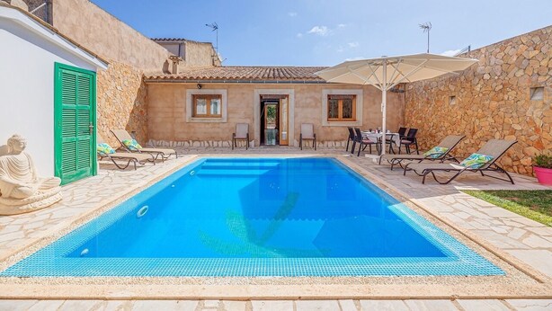 A swimming pool with lounge chairs and a Buddha statue, surrounded by stone walls and a tiled roof. - Casa Las Vías (Petra, Mallorca)
