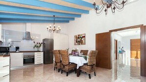 A modern kitchen with white cabinets, a stainless steel refrigerator, and a dining area with wicker chairs and a white tablecloth. - Casa Las Vías (Petra, Mallorca)