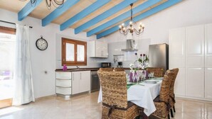 A modern kitchen with white cabinets, a stainless steel refrigerator, and a dining area with wicker chairs and a white tablecloth. - Casa Las Vías (Petra, Mallorca)